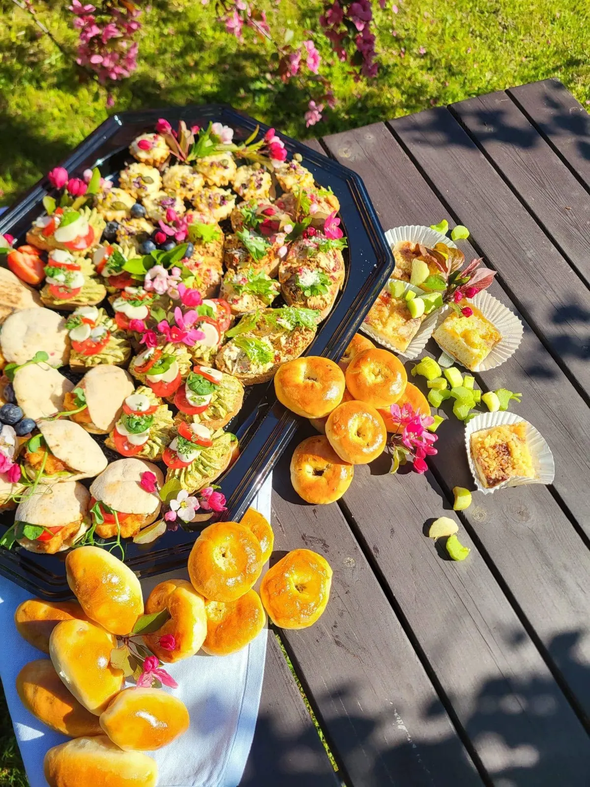 Uzkodu plate, pīrādziņi un rabarberu kūka uz koka galda dārzā